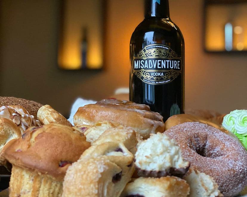 A bottle of Misadventure & Co vodka, which is made from pastries and baked goods, surrounded by pastries and baked goods.