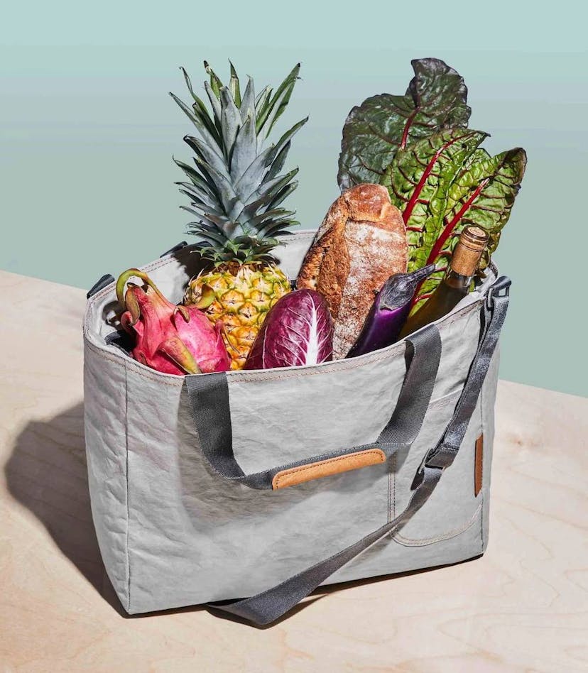 A gray cooler bag with vegetables, fruit, and a bottle of wine inside