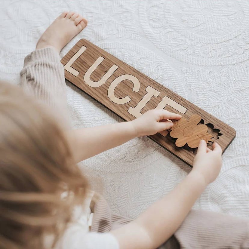 A baby is shown from overhead playing with a wooden puzzle toy that spells out the name Lucie.