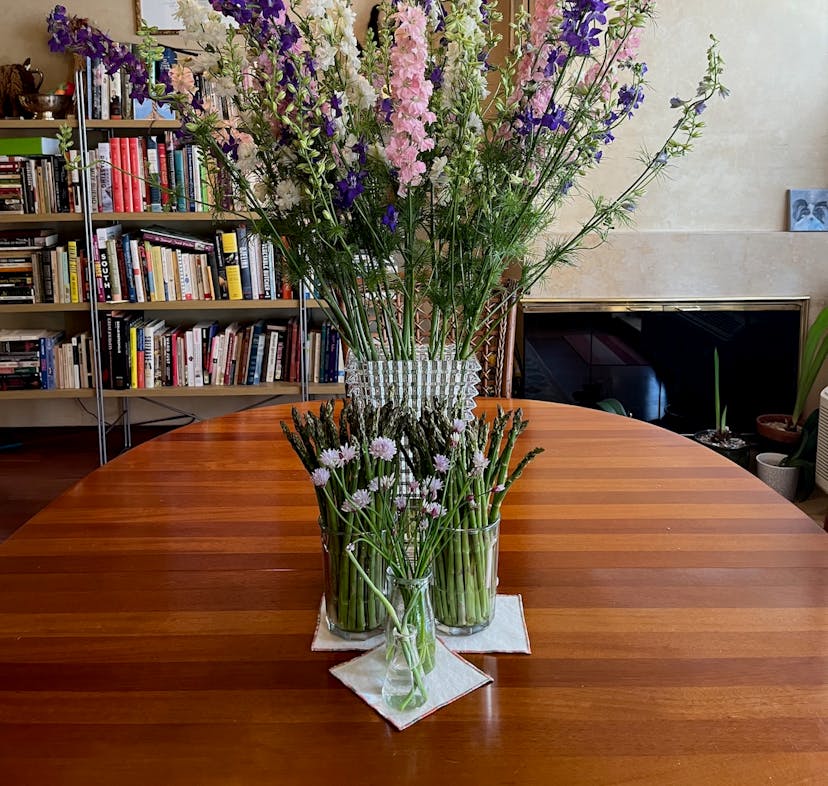 A wood dining room table with glass and crystal vases on top and bookcases in the background.
