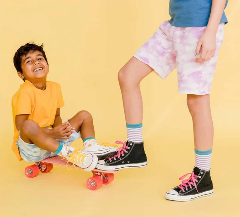 A young kid grins and sits on a skateboard being pushed by an older boy.