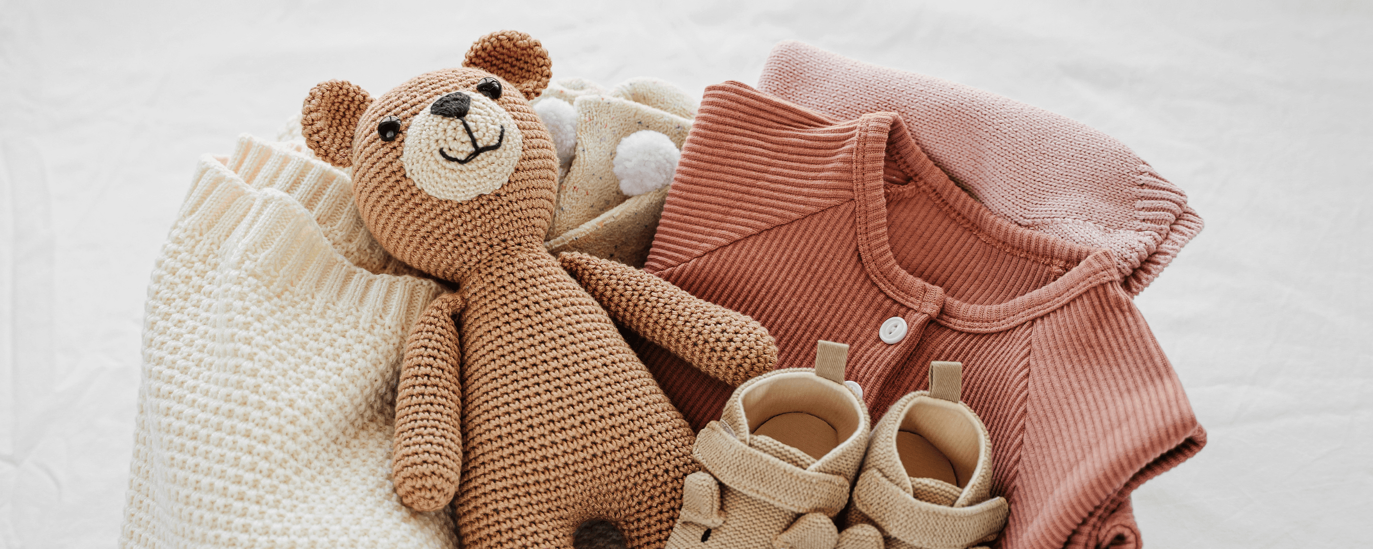 A teddy bear among a collection of sustainable kids and babies apparel.