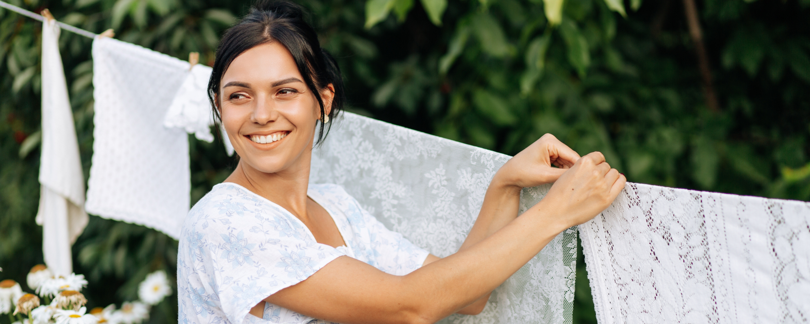 A smiling woman hanging laundry outdoors.