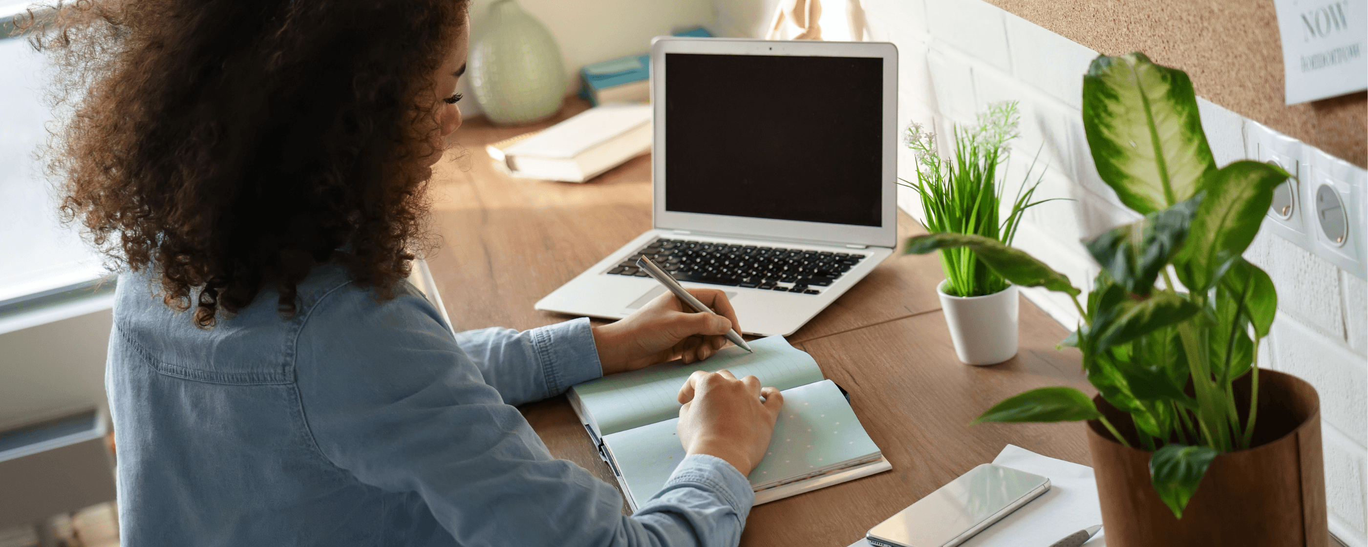 A woman taking notes in front of a laptop at a home office.