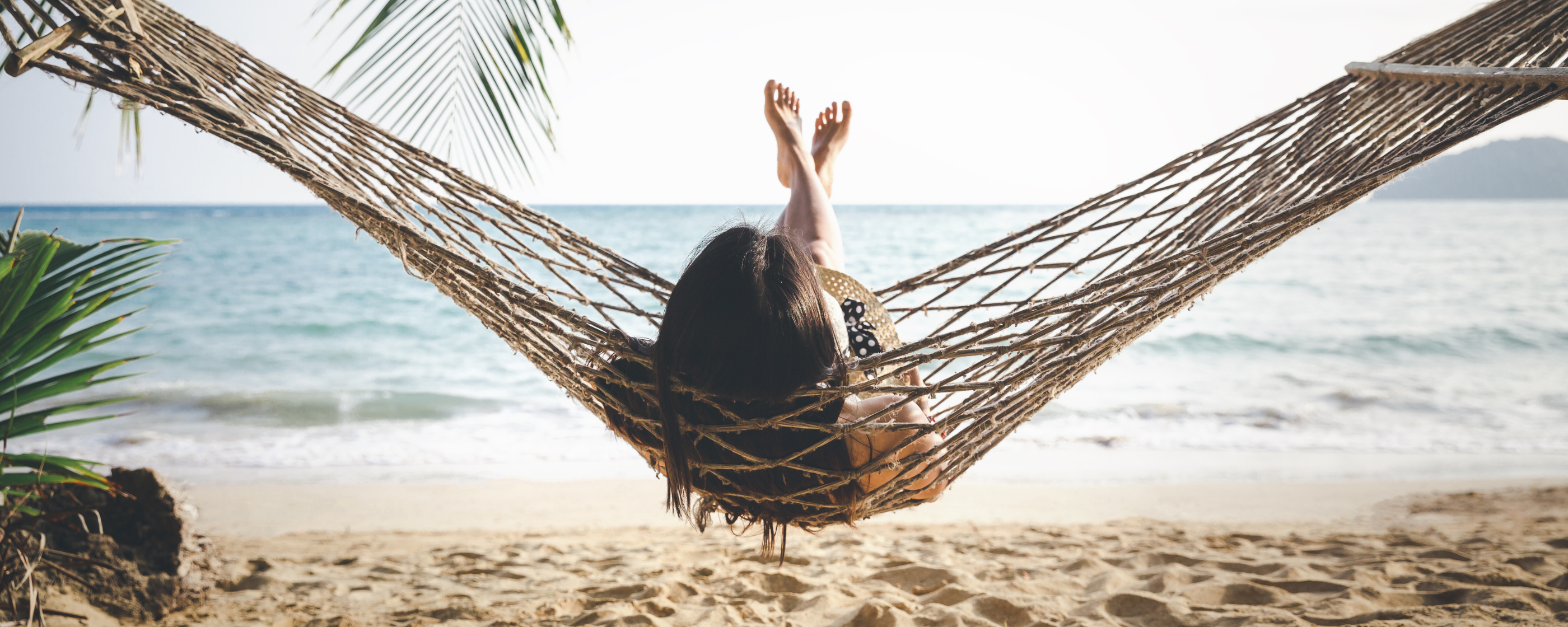 A woman with her feet up on a hammock on a beach.