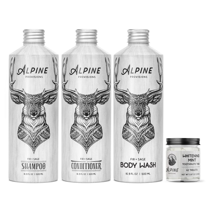 Three aluminum bottles, each with a line drawing of a deer on them and the brand name Alpine Provisions and the size noted as 16.9 ounces. One is a shampoo, one a conditioner, one a body wash, all in the Fir + Sage scent. A small glass bottle with a black top to the right, filled with white tablets, is labeled with the same Alpine Provisions brand, as well as “Whitening Mint Toothpaste Tabs.”