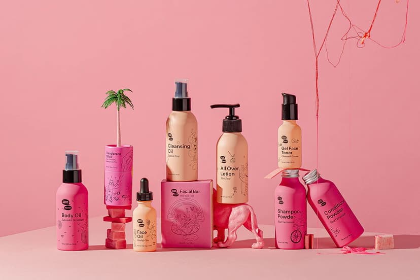 An assortment of Meow Meow Tweet brand products for face and body, all packaged in bright and light pink metal bottles and cardboard tubes.