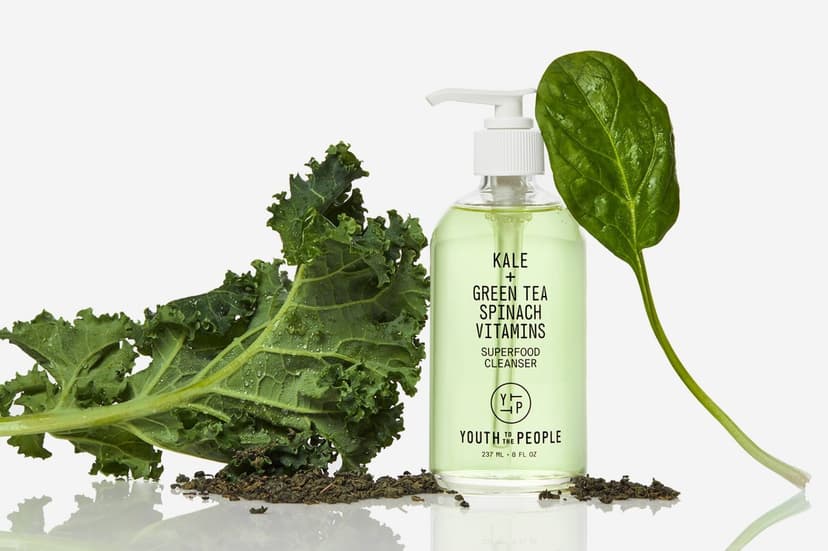 A clear glass bottle of light green liquid in between a kale leaf and a spinach leaf. The bottle reads “Youth to the People Kale + Green Tea Spinach Vitamins Superfood Cleanser”