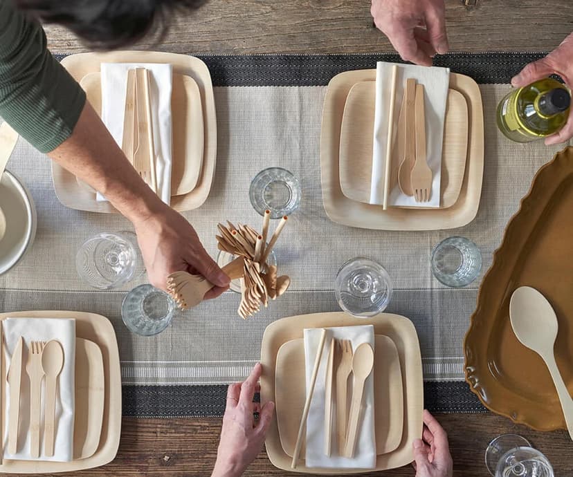 A dining table shown above, set with bamboo plates, straws and utensils.