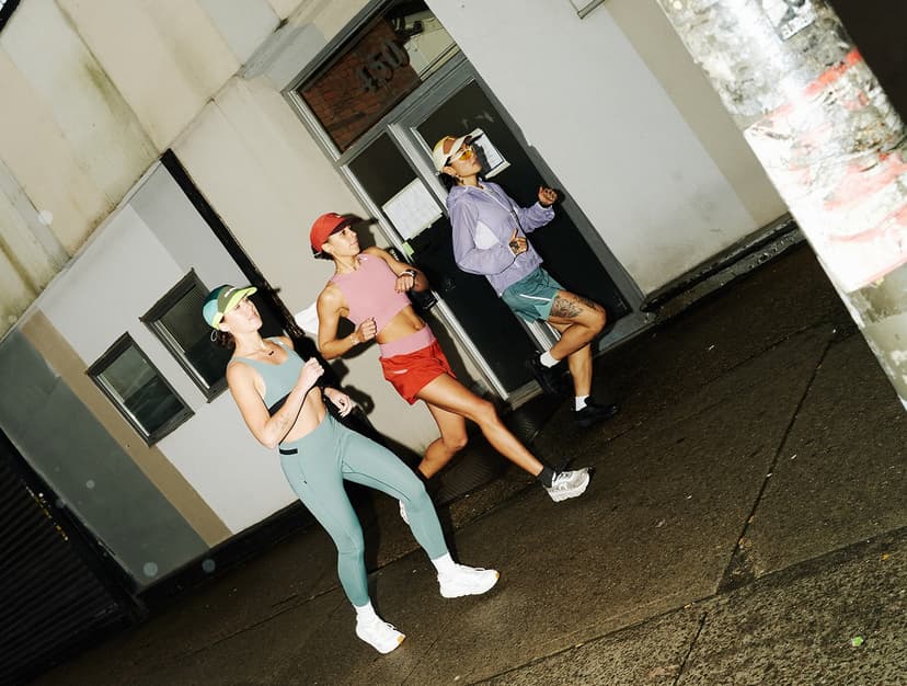 Three women running on an urban sidewalk in colorful clothes.