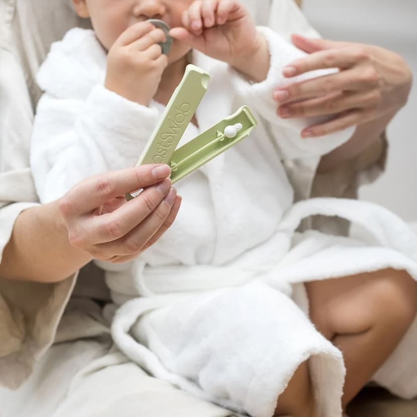 A person holds a baby in a white robe on her lap and holds a light green case with a nubby ear swab inside. The case reads LastSwab.