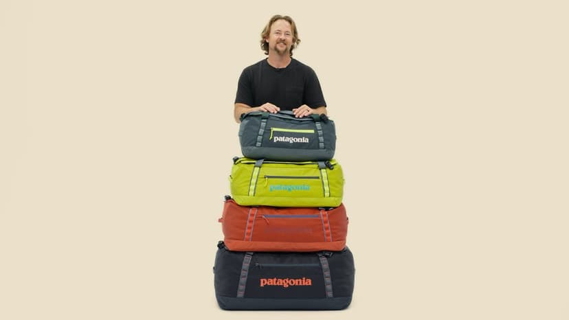 A man standing in front of a pile of four duffel bag suitcases of descending size, all labeled with the brand name Patagonia. The bags are made by sustainable clothing and sustainable luggage brand Patagonia.