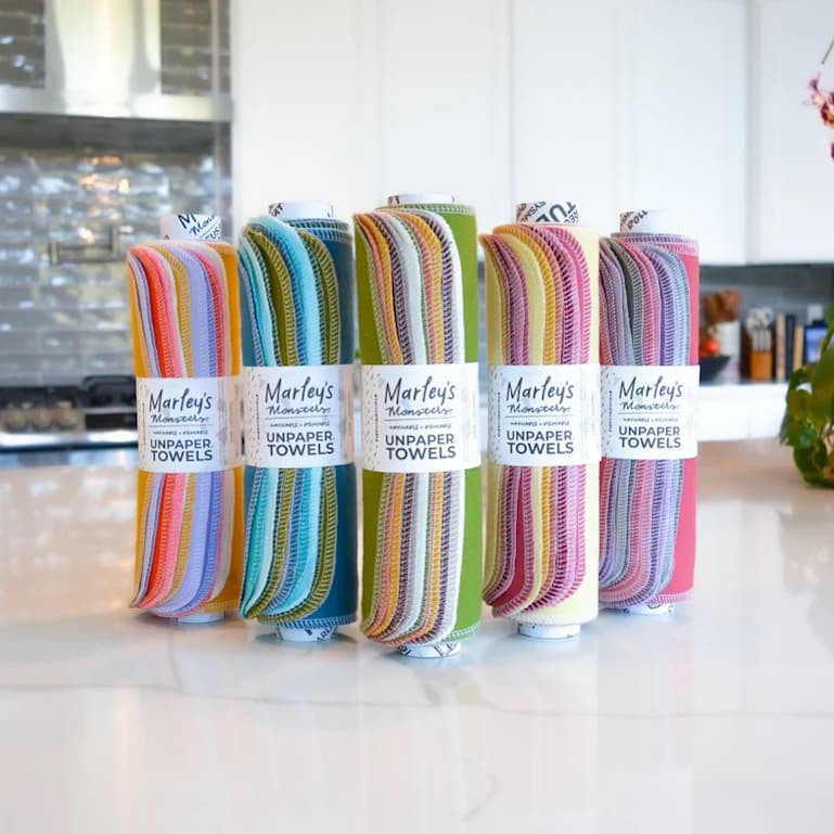 Five tubes with rolls of color fabric wrapped around them on a kitchen counter. The fabric rolls all have labels that read "Marley's Monsters Unpaper Towels"