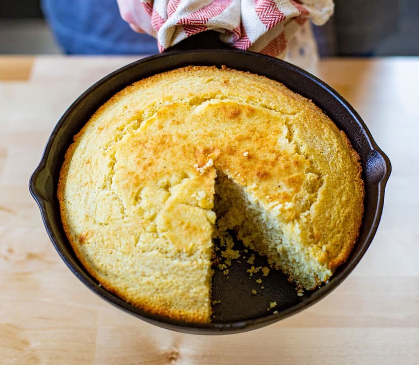A large cast iron skillet with a cooked cornbread with one slice missing.