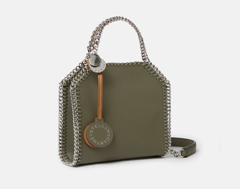 A small olive green purse with a silver chain strap and a round silver keychain with the words Stella McCartney printed on it.