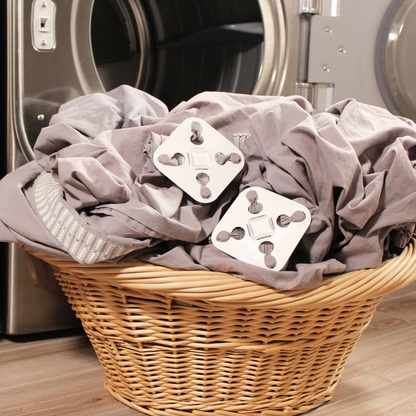 An open laundry machine with a wicker laundry basket in front of it. The baske has grey bed linens in it, with two white plastic squares on top of the bed linens.