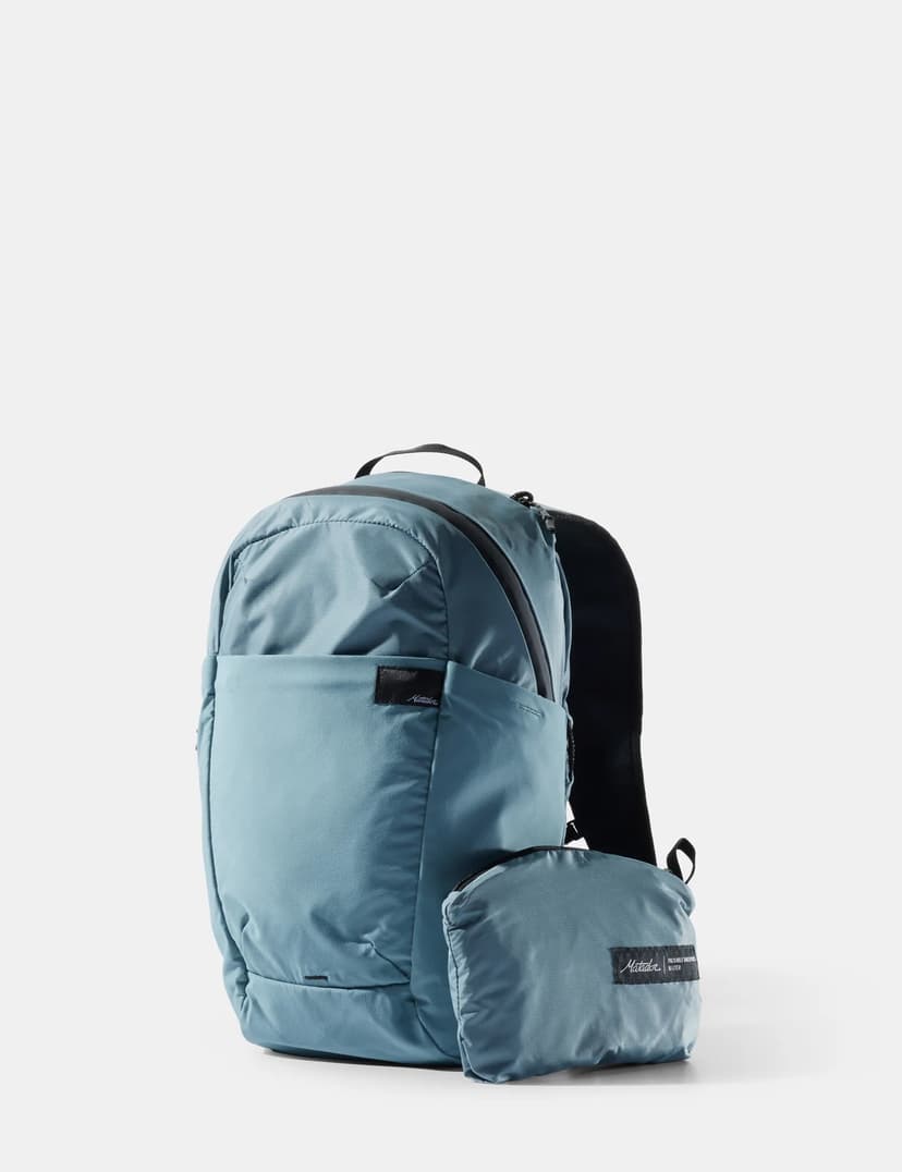 a blue backpack made by matador equipment shown with a little bag in front of fit that the backpack can compress down into.